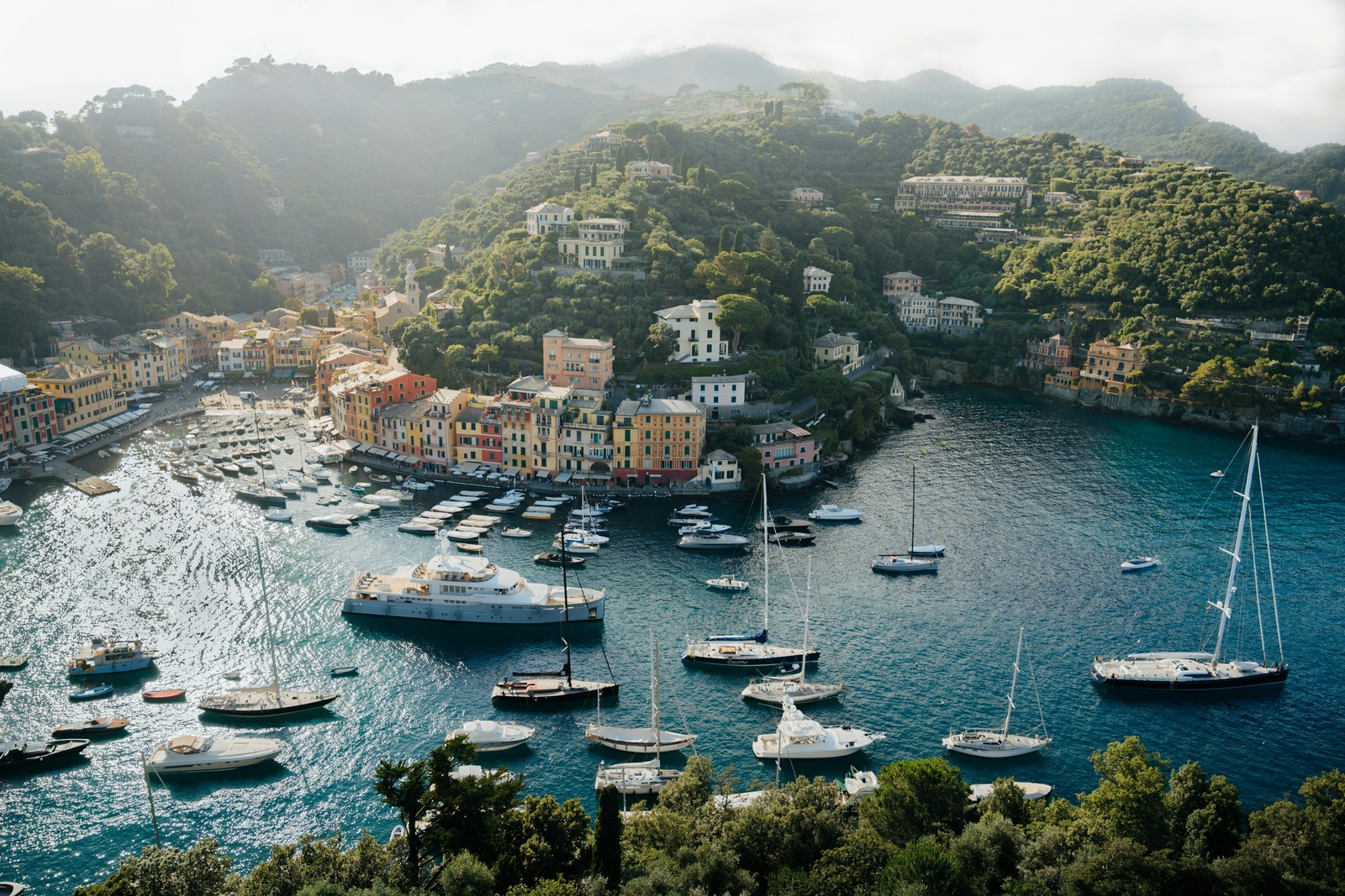 The colorful harbor of Portofino sits along the Ligurian coast, framed by green hills and dotted with yachts on the calm Mediterranean sea. Photo by Peter Thomas.