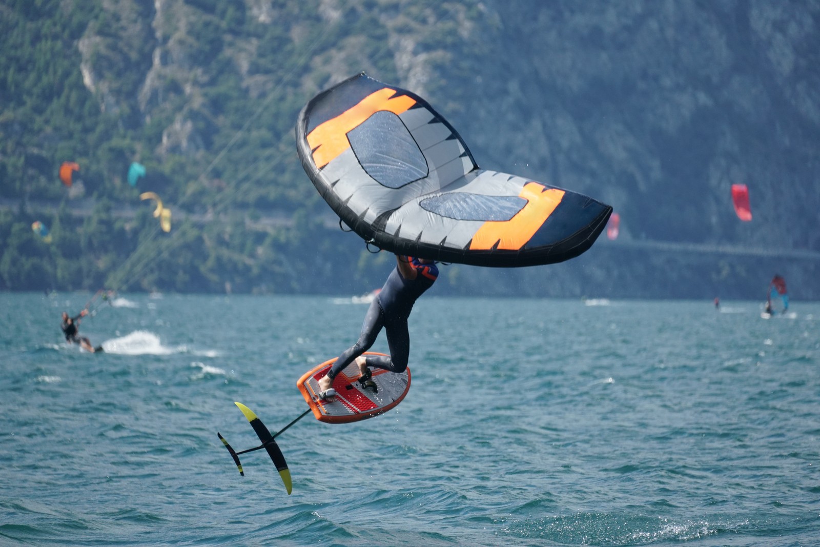 A thrill-seeker catches air while wing foiling on Lake Garda near Riva del Garda, surrounded by fellow wind and kite surfers in one of Italy’s top spots for water sports and adventure.